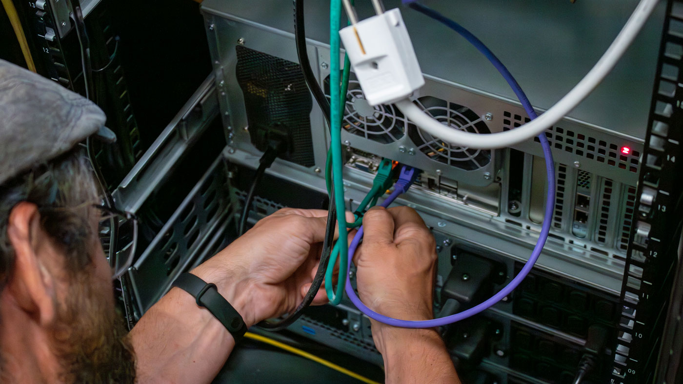 person in hat plugging in cables on a server (Photo)